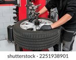 Small photo of High angle of anonymous male technician in casual clothes and gloves turning screws on disc while dismantling tire during work in garage