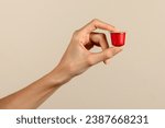 From above of anonymous young female holding coffee capsule in manicured slender index and thumb fingers and demonstrating against beige background