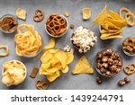 Assortment of Unhealthy Snacks: chips, popcorn, nachos, pretzels, onion rings in bowls, top view, copy space. Unhealthy eating concept.