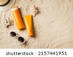 Small photo of Sunscreen lotion, sunblock cream, sunglasses and hat on sandy beach as background, top view, copy space. Summer vacation and skin care concept, spf uv-protect cosmetic products.