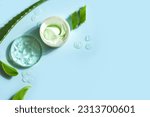 Aloe vera plant leaves and cosmetic gel for skin care  on blue background, top view, copy space. Natural organic aloe vera cosmetic gel in petri dish.