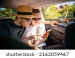 Young cheerful happy couple of travelers sitting in car looking at smartphone screen, travel comfort safety taxi concept