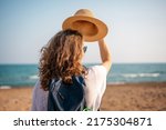 Portrait Young cheerful woman with a backpack putting on a hat on the seashore