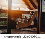 Young relaxed cheerful woman enjoying nature on the balcony of the cottage at sunset with a cup of tea