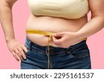 Small photo of Cropped midsection of an obese woman measuring her waist with a measuring tape against a pink background