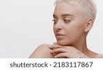 Small photo of Pretty slim young Caucasian woman with fair hair touches her jawline and shoulder looking away on white background | Sagging jowls prevention concept
