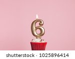 Number 6 gold candle in a cupcake against a pastel pink background
