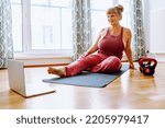 Small photo of middle-aged woman with curvaceous, plump, blonde, sits on sports mat, does yoga, sports, at home oline. Active lifestyle, keeping body in good shape for middle-aged women