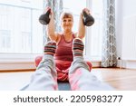 Small photo of middle-aged woman with curvaceous, plump, blonde, sits on sports mat, doing strength exercises with weights, along with teenager. Active lifestyle, keeping body in good shape for middle-aged women