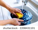 Women's hands wash dirty plate with sponge for dishes under stream of water from tap. concept of cleaning dirty dishes after eating, household chores, kitchen sink, water consumption
