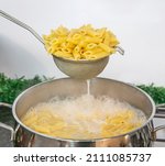 Small photo of Cooking Pasta pour the penne pasta into a metal pot of boiling water. Boiled penne on a steel colander, in a cooking class.