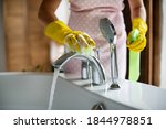 Professional cleaning of the bathroom and toilet. Cleanliness and hygiene at home. Cleaning service and housekeeping. Hand in green and yellow latex gloves. Rubbing the bathroom and taps