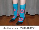 female feet in bizarre giraffe blue socks with pink donuts and classical black shoes, eclectic style