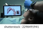 Small photo of Doctor scans the patient's teeth in the clinic. The dentist holds in his hand a manual 3D scanner for the jaw and mouth. Dental health. Creates a 3D model of teeth and gums on a medical monitor.