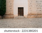 A historic church door in a latin village architecture style, that could be from Europe or America, surrounded by a road, garden wall and trees. Backdrop for graphic resource or decorative copy space.