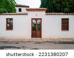A rustic door in a latin village architecture style, that could be from Europe or America, surrounded by a road, garden wall and trees. Backdrop for graphic resource or decorative copy space.