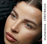 Small photo of Cosmetician in gloves making white markup before brow permanent procedure at beauty salon