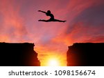 Small photo of Silhouette of girl dancer in a split leap over dangerous cliffs with sunset or sunrise background and copy space. Concept of faith, conquering adversity, taking risk; challenge, courage, determination