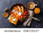 English breakfast in pan with fried eggs, sausages, bacon, beans, toasts and coffee on dark stone background