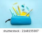 Top view of pencil case with school supplies on blue background. Back to school concept