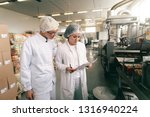 Two quality professionals in white sterile uniforms checking quality of salt sticks while standing in food factory.