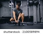 Small photo of Preparing for strong muscle burning training. A young attractive man in gray sportswear sets up barbell weights in the gym. Fit young man looking focused on practice, sports discipline