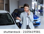 Small photo of Smiling female car seller having phone conversation with a client and convincing him to buy a car. Car salon interior.