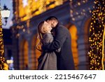 Christmas couple hugging and kissing on New Year's eve. A young happy couple is standing on the street surrounded by Christmas lights, hugging and kissing on Christmas eve.