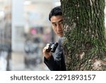 A man hiding in a tree and keeping a lookout with binoculars in the city.