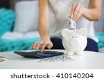 Female hand putting money into piggy bank and counting on calculator closeup