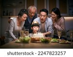 Small photo of little asian boy blowing candles while three generation family celebrating her birthday at home