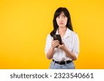 Small photo of Portrait female anxious scared on the phone seeing bad news, Young Asian beautiful woman wearing white shirt and denim plants shocked with mobile phone isolated on yellow background. Bad news concept.