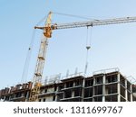 Industrial crane near building against blue sky. Commercial construction project. Construction site.