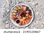 Mussels in shells, squid in a bowl, octopus, shrimps with lemon, thyme and onions in a plate standing on a white wooden table with shells and stones