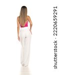 Small photo of back view of a young modern woman in white pants and pink corset posing on white studio background
