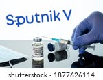 Small photo of Morgantown, WV - 16 December 2020: Small bottle of coronavirus vaccine with syringe with background of Russian Sputnik V logo