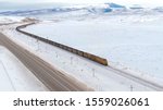 Small photo of DRONE: Locomotive transports a long line of railcars full of coal across the idyllic wintry United States. Freight train moves along a highway while transporting cargo from coal mine to storage depot.