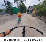POV: Riding a bicycle behind unrecognizable tourist girl exploring the scenic tropical island. Two young travelers riding their bikes around the idyllic rural villages on picturesque Himmafushi island