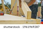 Small photo of CLOSE UP, DOF: Unrecognizable male builder picks up a CLT beam from a workbench at an unfinished housing project. Contractor carries a glued laminated board across the bustling construction site