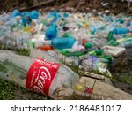 Small photo of TIRANA, ALBANIA, MARCH 2022: Ironic image of plastic Coca Cola bottle with waste pollution at river. Inappropriate place for garbage disposal. Accumulated plastic garbage floating on river surface.