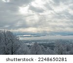 Sun rays shine through receding storm clouds rolling across snowy countryside. Incredible view from hilltop over hilly landscape covered with freshly fallen snow. Idyllic winter moment after snowstorm