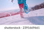 Small photo of LENS FLARE, CLOSE UP: Playful woman snowshoeing on a snowy meadow above valley. She enjoys freshly fallen snow on a nice sunny day as she runs in snowshoes. Flying snowflakes sparkle in winter sun.