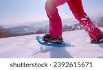 Small photo of LENS FLARE, CLOSE UP: Active young woman is running with snowshoes on fresh snow on a beautiful sunny winter day. White snowflakes spray and sparkle in sunlight as she lifts her feet while snowshoeing