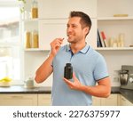Small photo of Man in bright kitchen prepares to swallow pill - could be medication or vitamins. Determined expression suggests discomfort. Emphasizes self-care and importance of wellness.