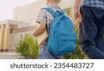 Small photo of Child Schoolboy walking down street with backpack, holding his dad by hand. Happy family, father, child go to school together. Dad is taking his little son with textbook to school. Preschool education