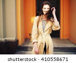 Young stylish hipster girl wearing modern trench coat walking in urban city smiling happy. Caucasian female model in her 20s.