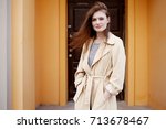 Young stylish hipster girl wearing modern trench coat walking in urban city smiling happy. Caucasian female model in her 20s. Fall fashion