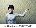 Small photo of Vintage presentation of generic object copyspace. Woman in bowler hat, white shirt, black bow tie, extends arm to show. With an indifferent, nonchalant expression against yellow-green wallpaper