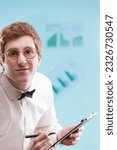 Small photo of In focus, a young man with a nerdy, subservient vibe, wears a dated office suit and holds a notepad. His white shirt, bowtie, and sad gaze hint at an accountant's life