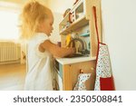 Small photo of small child plays with shrunken versions of household appliances and furniture, such as a sink, kitchen, drying racks for saucers